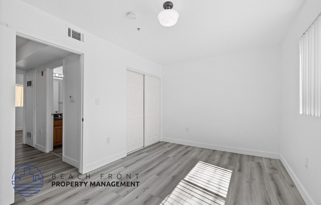 a bedroom with white walls and wood flooring and a door to a bathroom