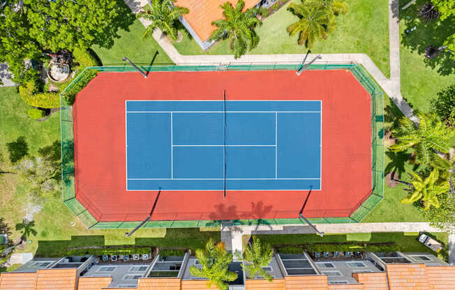 A tennis court is surrounded by trees and buildings.