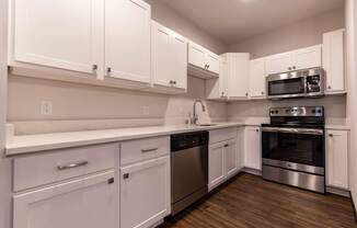 A bright modern kitchen here at The Park with white shaker cabinets, stainless steel appliances, long quartz counters, and warm wood floors, creating a clean, stylish, and inviting cooking space.
