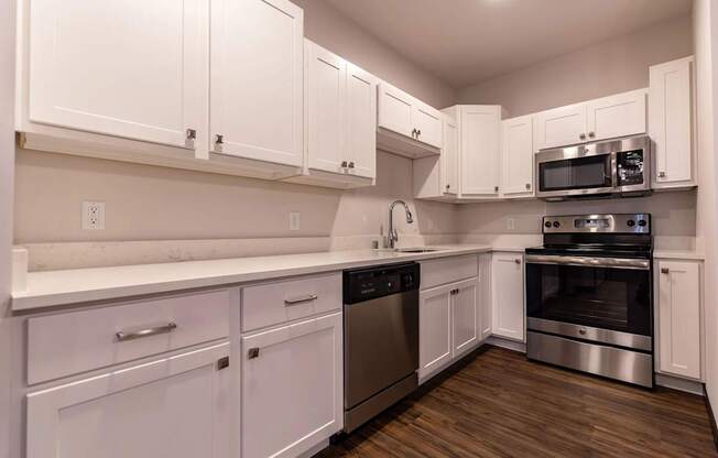 A bright modern kitchen here at The Park with white shaker cabinets, stainless steel appliances, long quartz counters, and warm wood floors, creating a clean, stylish, and inviting cooking space.