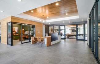 a modern clubhouse lobby with a large free floating stone and wood desk, between two offices with floor to ceiling windows