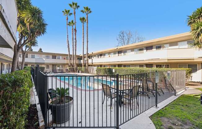 A pool surrounded by a black fence with a building in the background.