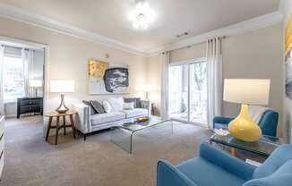 A living room with a grey couch, a blue armchair, a glass coffee table, and a yellow lamp.