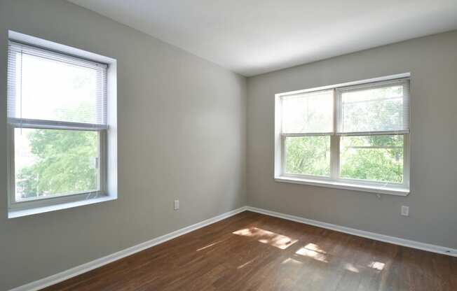 an empty room with two windows and a hardwood floor