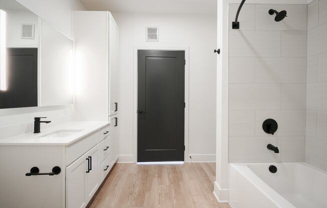 a bathroom with white cabinets and a black door     and a shower