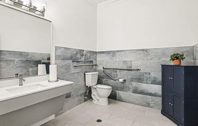 A bathroom with a white sink, toilet, and a grey tiled wall.