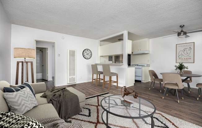 a living room with a couch a table and chairs and a kitchen in the background