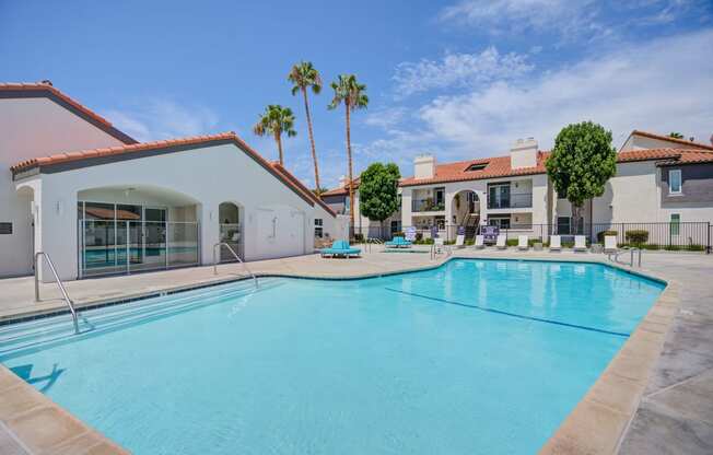 a large swimming pool with lounge chairs and palm trees in the background  at Laguna Gardens Apts., Laguna Niguel, California