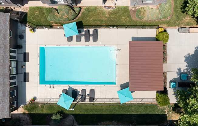 A swimming pool surrounded by chairs and a brown building.