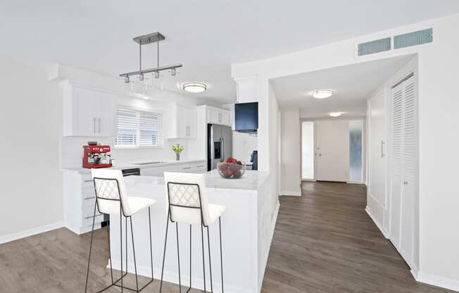a kitchen with white cabinetry and a white island with three white chairs