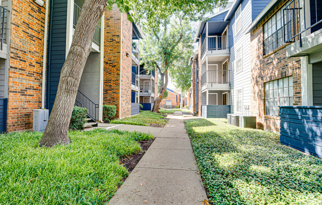 a sidewalk between two apartment buildings with grass and trees