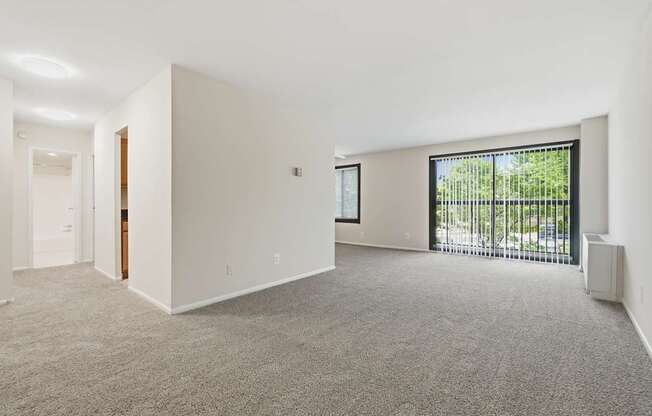 A large, empty room with a carpeted floor and a window with blinds.