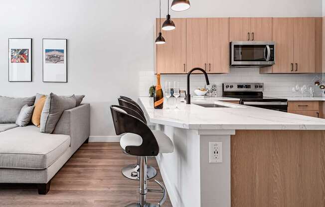 A modern kitchen with a white countertop and a grey couch with orange pillows.