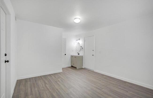 A room with a wooden floor and a white wall with a cabinet and a mirror.