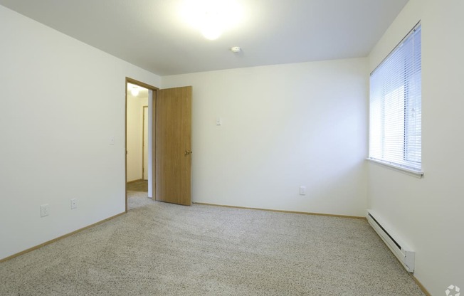 A room with a carpeted floor, a door, and a window with blinds.