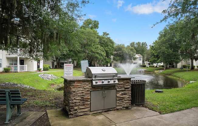 A BBQ grill is in the middle of a grassy area with a sign in front of it.