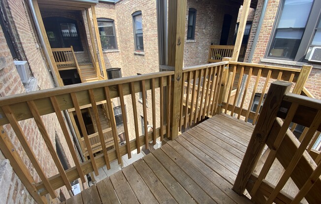 the back deck of a brick apartment building with a wooden railing