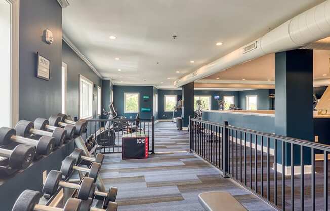 a fitness room with cardio machines and chairs at the bottom of a staircase