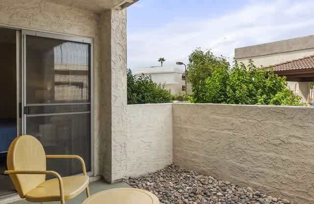A yellow chair and table are on a patio with a view of a building and trees.