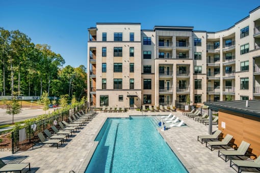 a swimming pool with lounge chairs in front of an apartment building