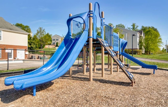 A blue slide in a playground with a wooden structure.