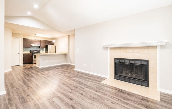 A living room with a fireplace and a kitchen in the background.