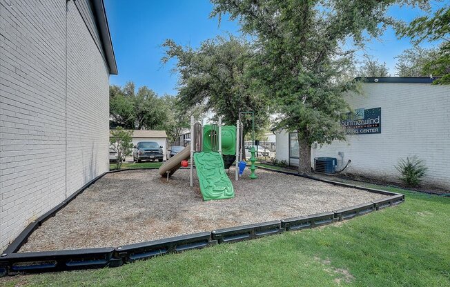 a playground with a slide and climbing equipment in a yard next to a white building