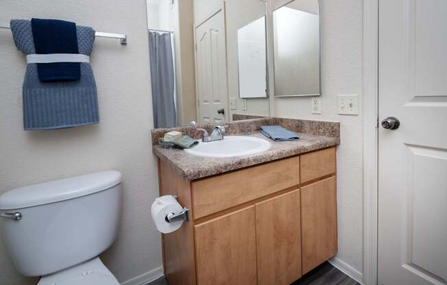 A bathroom with a white toilet, wooden cabinets, and a blue towel hanging on the wall.