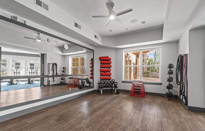A spacious room with a ceiling fan, exercise equipment, and a view of the outdoors through large windows.
