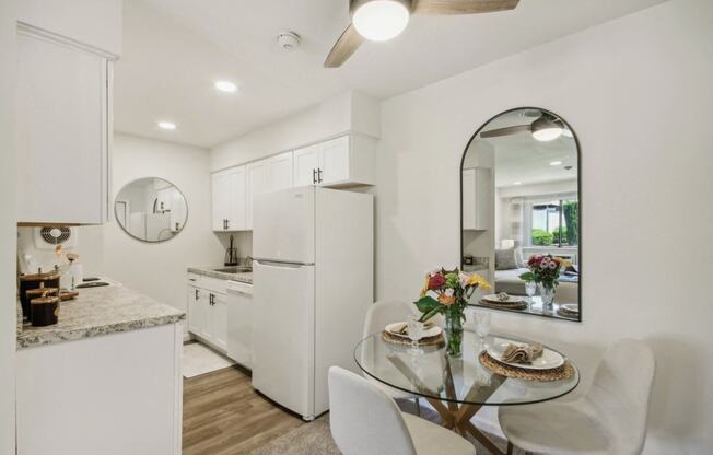 a white kitchen  with granite counter top and dining area with a glass table and chairs