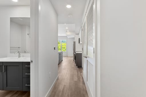 a long hallway with white walls and wood flooring and a kitchen with a sink
