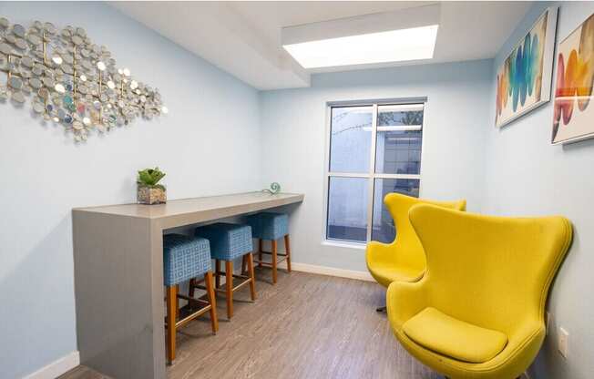 A yellow chair is in front of a grey desk with a plant on it.