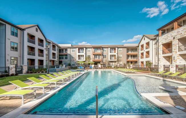 a swimming pool with yellow lounge chairs in front of an apartment building