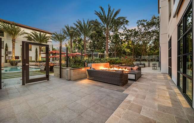 Fire pit lounge with woven seating, glowing flames, and palm-lined views creating a resort-style retreat