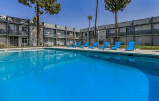 A swimming pool with blue water and lounge chairs in front of a building.
