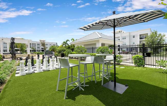 A table and chairs set up on a lawn with a chess board in the middle.