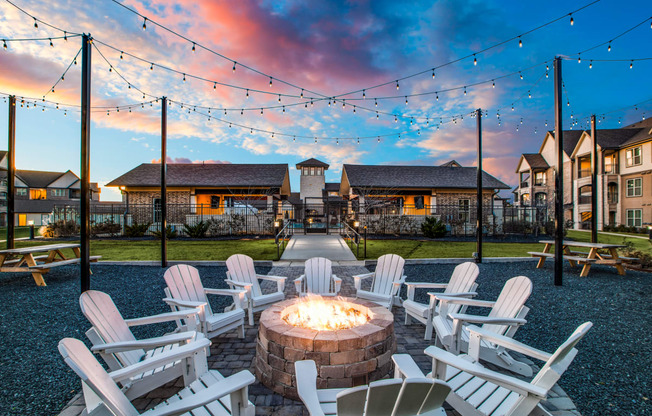 a fire pit with white rocking chairs and string lights