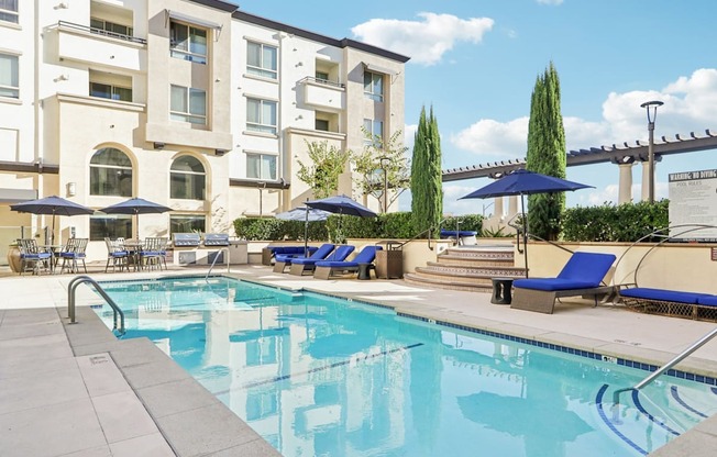 A swimming pool with blue loungers and umbrellas in front of a building.