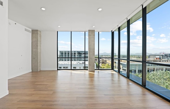 A large empty room with wooden floors and a view of the city through large windows.