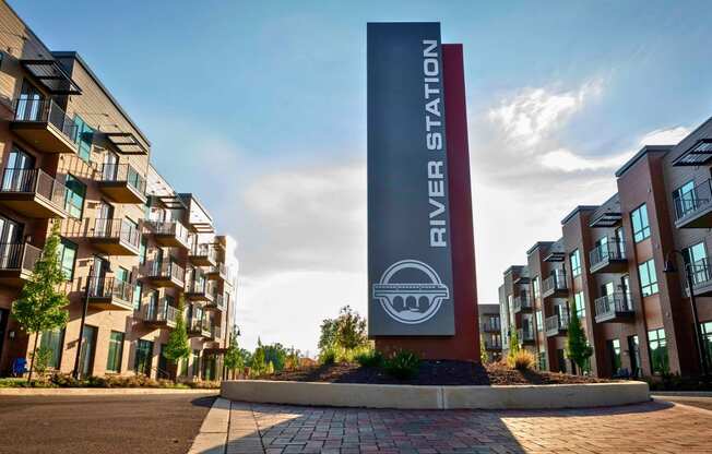 A River Station sign in front of modern apartment buildings with balconies and trees lining a street.