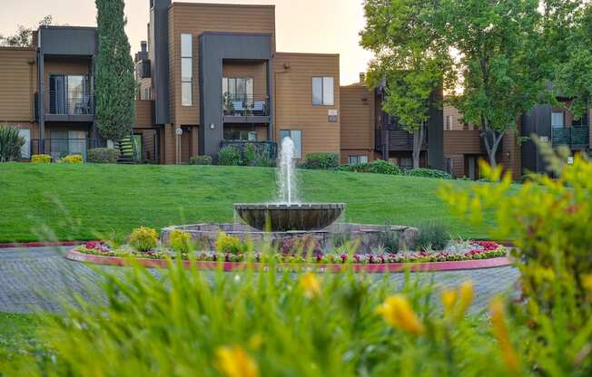 A fountain in the middle of a garden in front of apartment buildings.