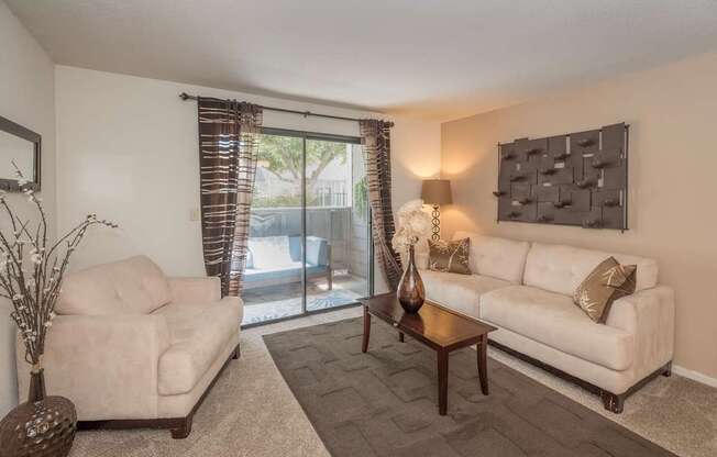 A living room with a white couch, a chair, a table, and a vase on the table at Bishop's Court Apartments, California, 95670