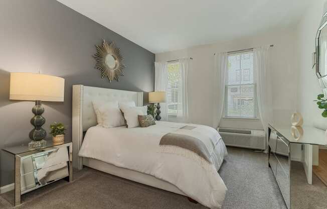 A bedroom with a large bed, a nightstand with a lamp, and a mirror on the wall.