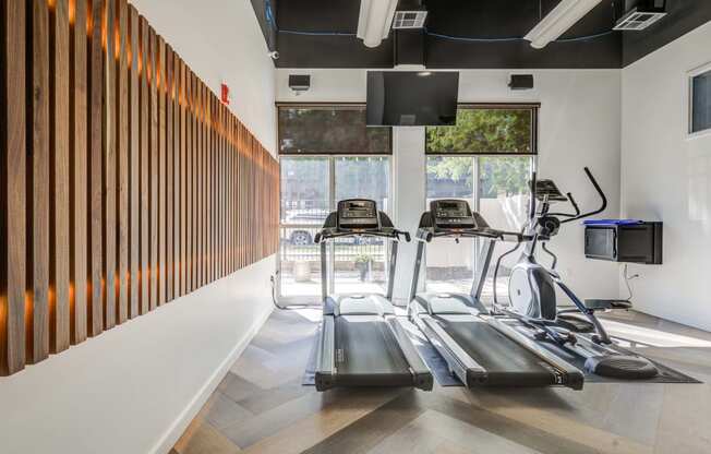 two treadmills in a gym with a window and a wall of wood panels
