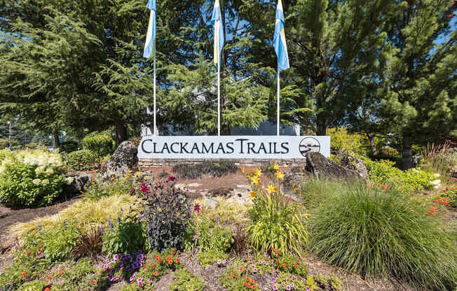 A sign that says Clackamas Trails stands in front of some trees and flags at Clackamas Trails Apartments, Oregon, 97222