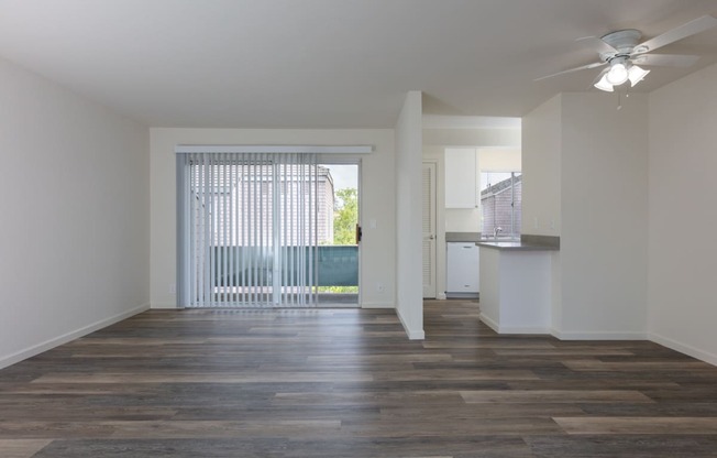 an empty living room and kitchen with wood flooring and a ceiling fan