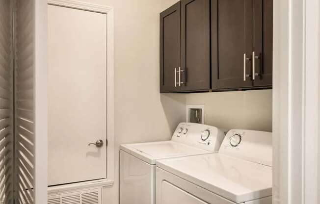 a laundry room with white appliances and dark cabinets  at Arlo Luxury homes Apartments, Arkansas