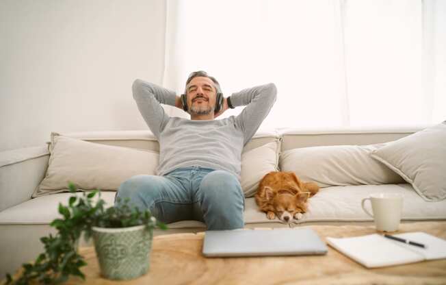 man on couch with dog listening to music on headphones