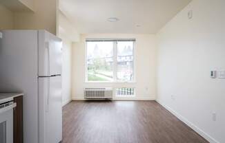an empty living room with a refrigerator and a window