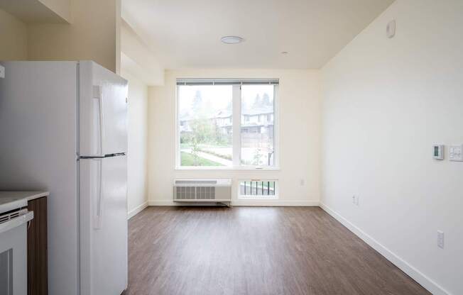 an empty living room with a refrigerator and a window